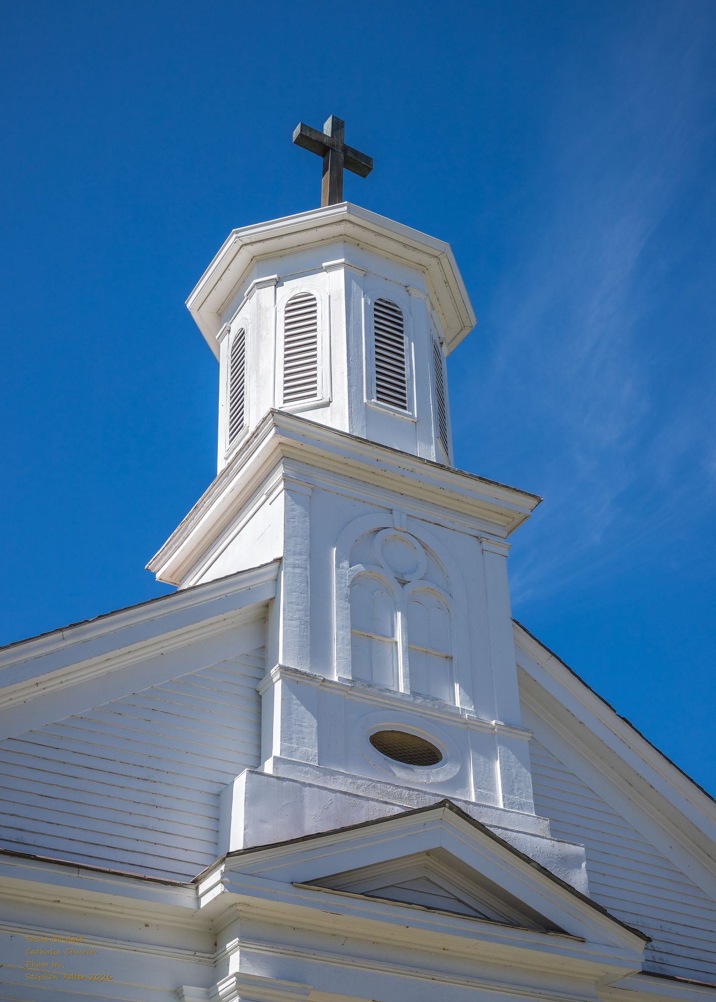 The steeple of St. Bridget Catholic Church against a blue sky